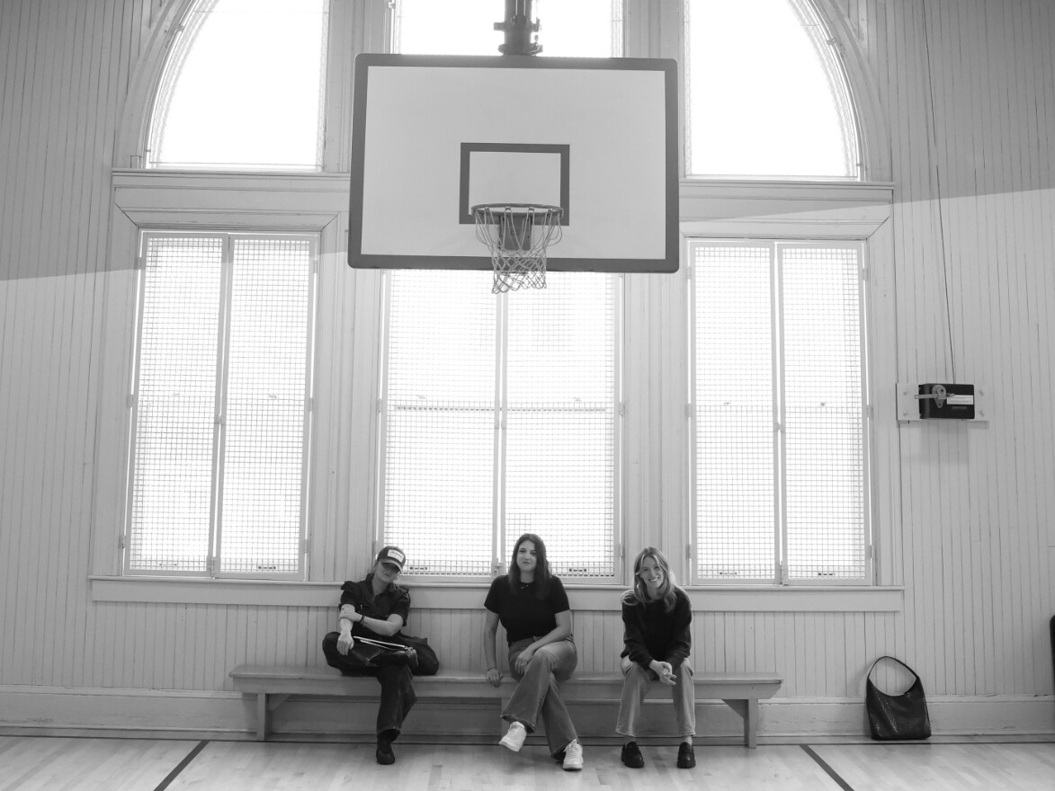 Three women sitting below a basketball hoop